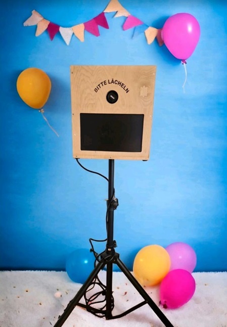 Eine Fotobox auf einer Veranstaltung mit buntem Hintergrund, Requisiten wie Hüten, Brillen und Schildern, bereit für Gäste, um lustige Fotos zu machen.